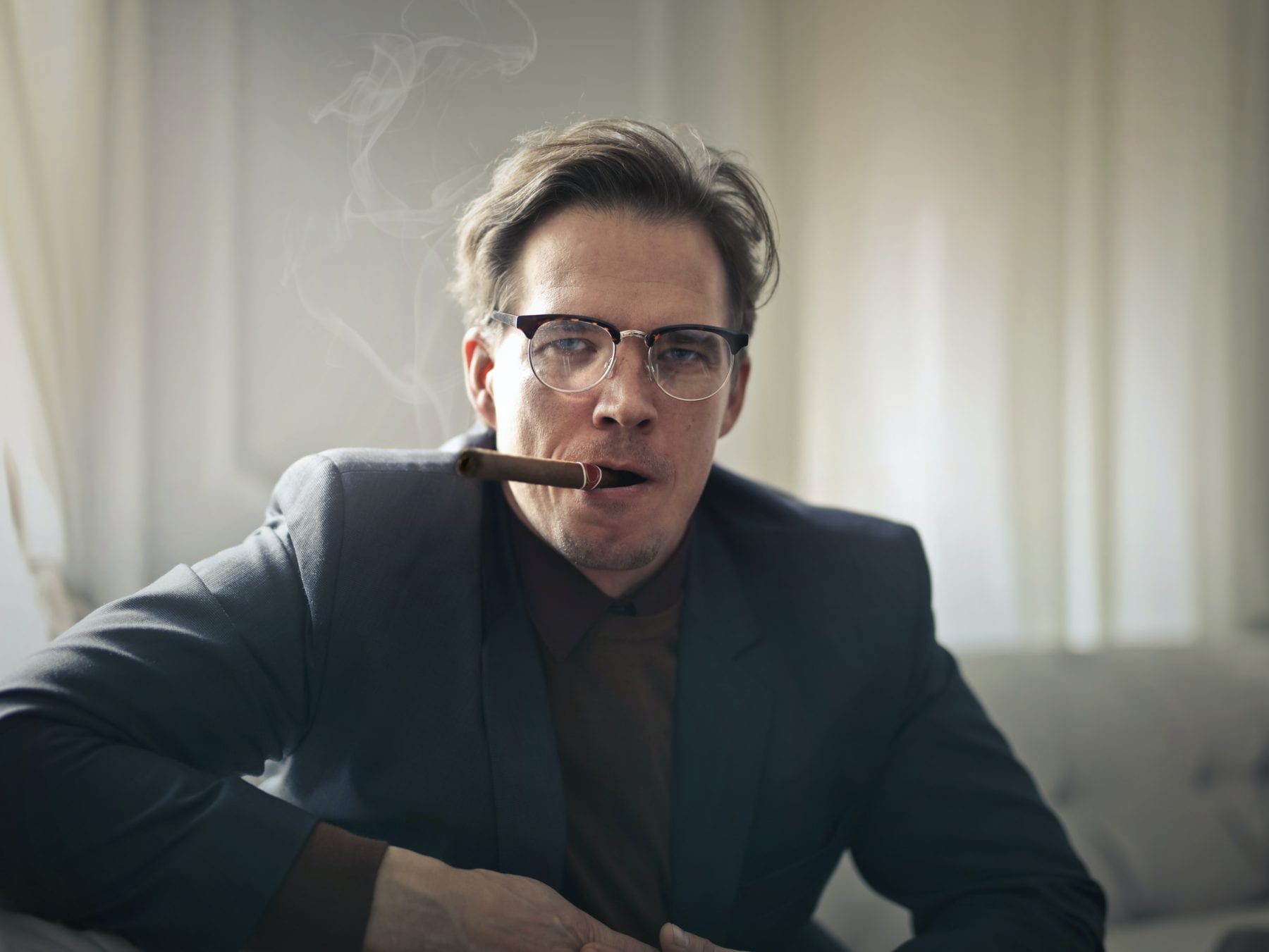 Man in black suit coat wearing eyeglasses Smoking Cigars